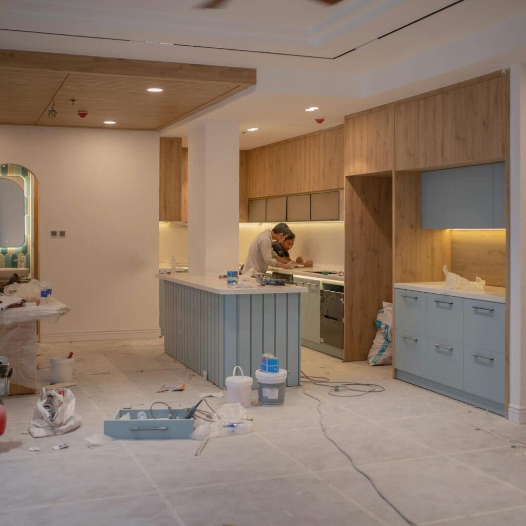 A modern kitchen undergoing renovation, featuring a worker, tools, and materials.